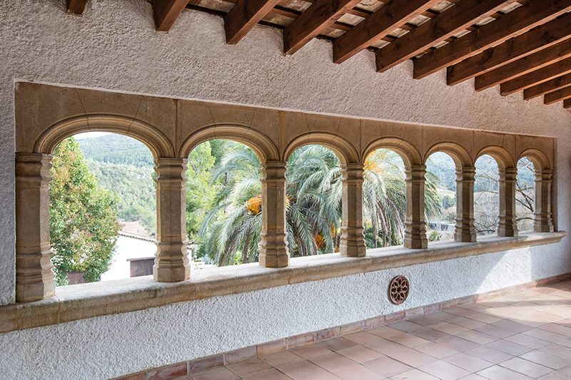 Stone arched gallery at Masia Torreblanca, with wooden beams and palm trees